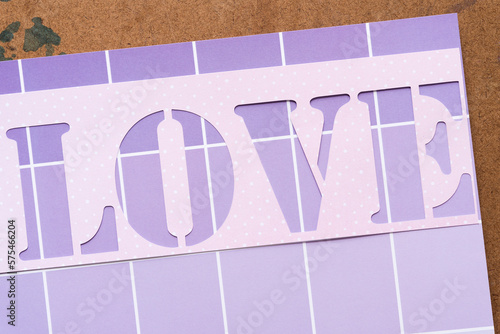 paper stencil with the word "love" on purple paper with squares and lines and old art board