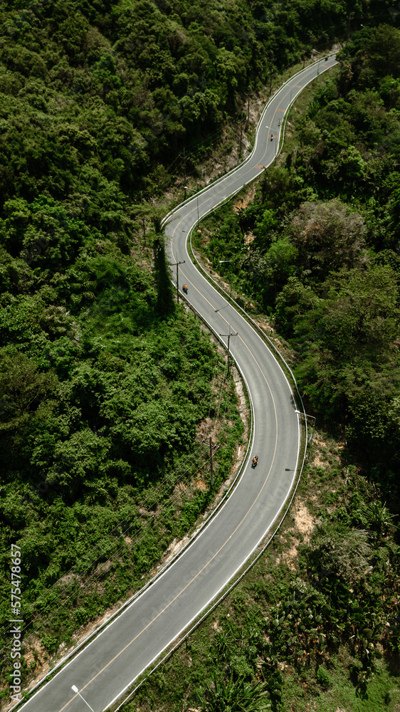 Top view of a country road in a green summer forest in the form of a winding curve with motorcycles. Rural landscape in Thailand. Aerial photography.