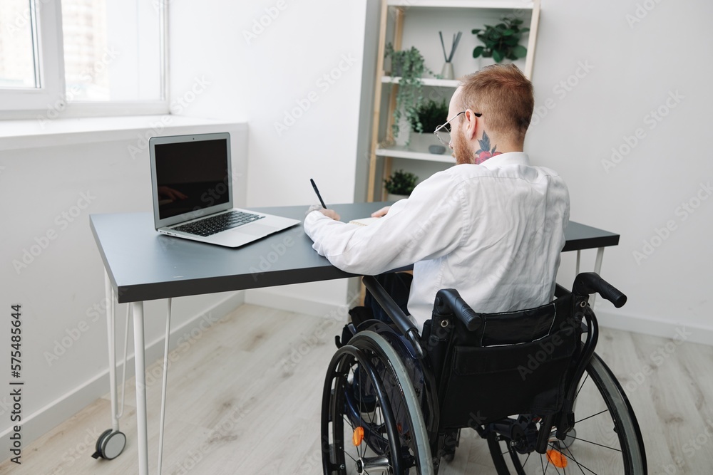 man wheelchair businessman with tattoos in the office works at a laptop online, business process from the back, copy space, integration into society, the concept of working a person with disabilities man wheelchair businessman with tattoos in the office works at a laptop online, business process from the back, copy space, integration into society, the concept of working a person with disabilities
