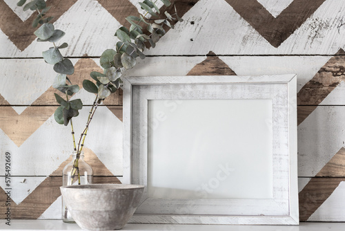 Blank, white picture frame mock-up farmhouse style with jar of eucalyptus and a decorative chevron wooden background