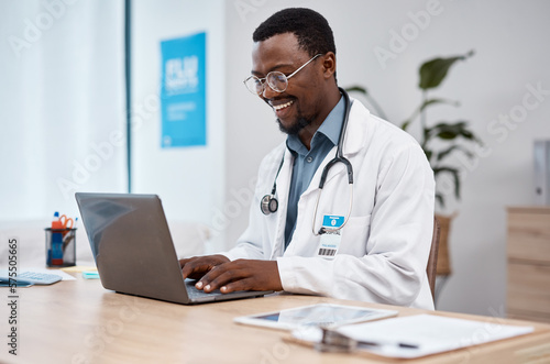 Black man  doctor and laptop with smile in healthcare for research  medicine or PHD at clinic desk. Happy African American male medical professional smiling  working or typing on computer at hospital