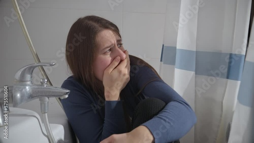 Afraid woman woman hiding in bathroom from criminal and closing her mouth with hand. Concept of domestic violence victim, stress, danger at home, fear.