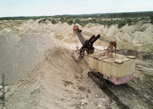 Dragline excavator digs chalk pile at large quarry in summer