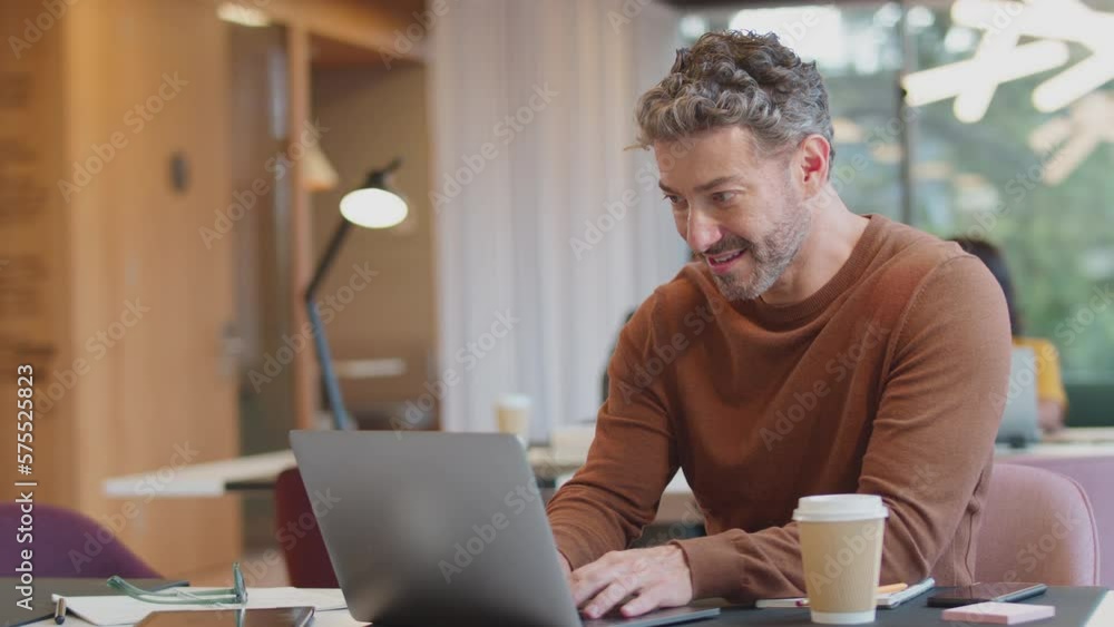 Mature businessman wearing glasses and working on laptop at desk in modern office - shot in slow motion Mature businessman wearing glasses and working on laptop at desk in modern office - shot in slow motion