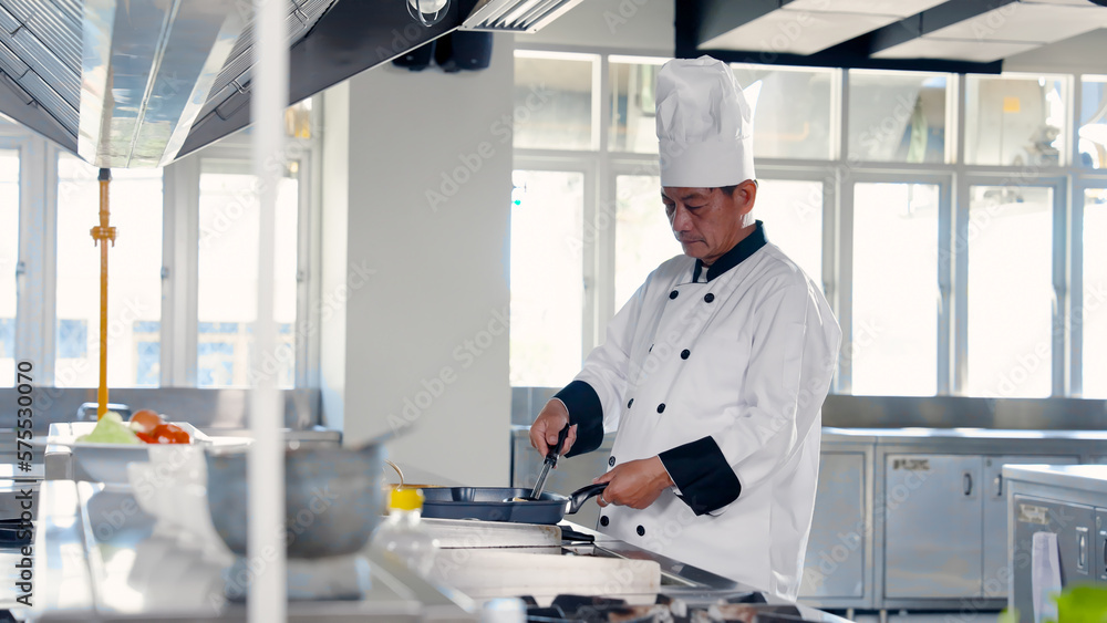 Naklejka premium Chef holding a golden ladle in a frying pan in the kitchen Prepare food for teaching students in cooking class. Learn to cook Thai food. on campus