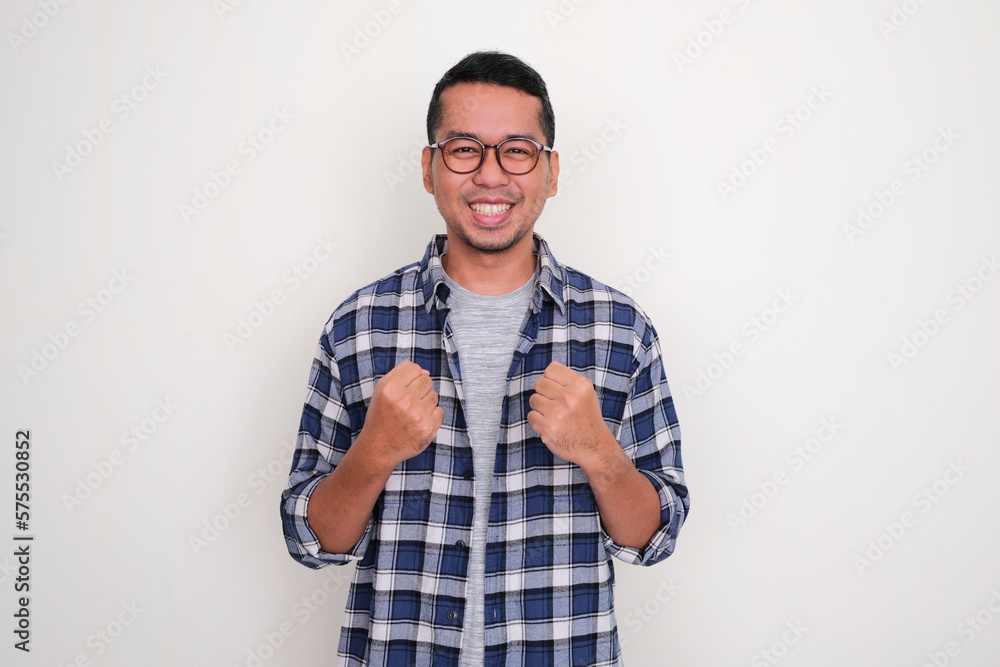 Adult Asian man smiling at the camera and clenching both hands showing excitement Adult Asian man smiling at the camera and clenching both hands showing excitement