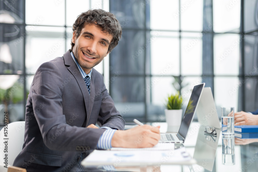 Portrait of young businessman sitting at his desk in the office. Portrait of young businessman sitting at his desk in the office.