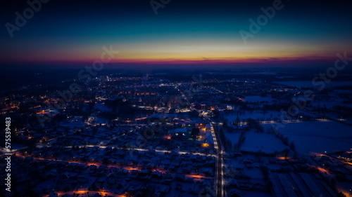 Flight over a city illuminated by a sunset flare. City lantern lights from above. A small town from above. Selective soft focus