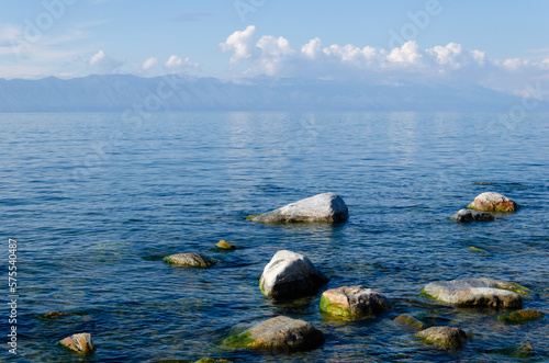The smooth surface of the water of Lake Baikal on a sunny summer day. Large stones in the water near the shore.