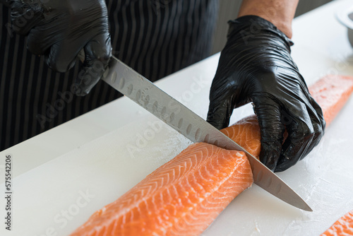 Japanese chef cleaning salmon. A worker cutting salmon on a board.