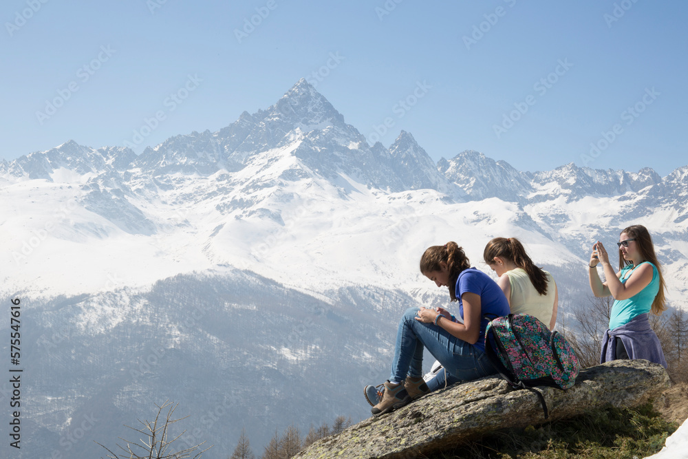 Three teen girls relax on rocks below mountain Three teen girls relax on rocks below mountain