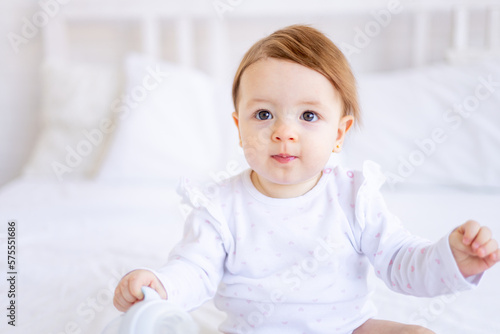 a large portrait of a cute and joyful baby girl in a crib in white clothes, a funny little child at home, the concept of children's goods