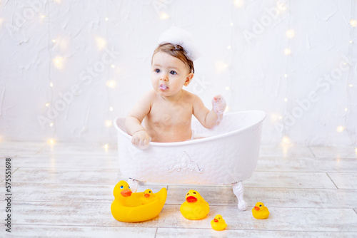 a joyful baby girl of six months is bathing in a bath with foam and rubber ducks, a small child is having fun playing with water, the concept of care and hygiene