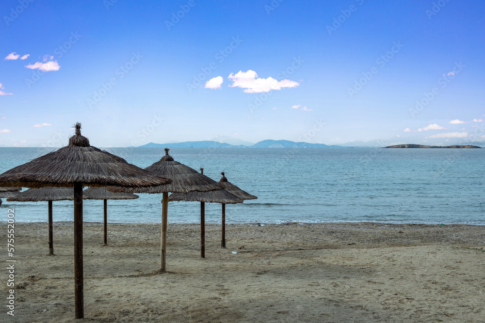 Straw parasol on empty sandy beach. Sea, blue sky background. Polluted seaside with plastic bottle. Straw parasol on empty sandy beach. Sea, blue sky background. Polluted seaside with plastic bottle.