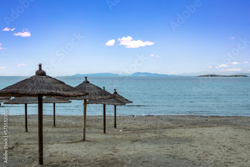 Straw parasol on empty sandy beach. Sea  blue sky background. Polluted seaside with plastic bottle.