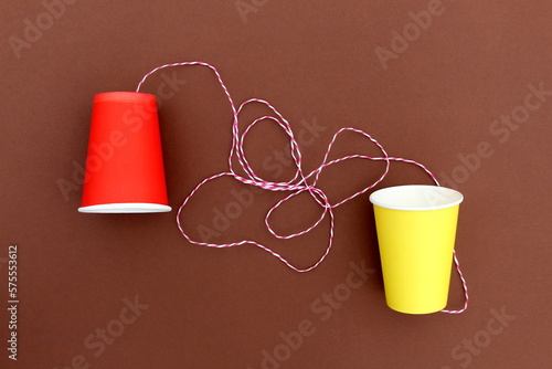 Schilderij op canvas An impromptu telephone made of bright paper glasses with a rope on a brown background