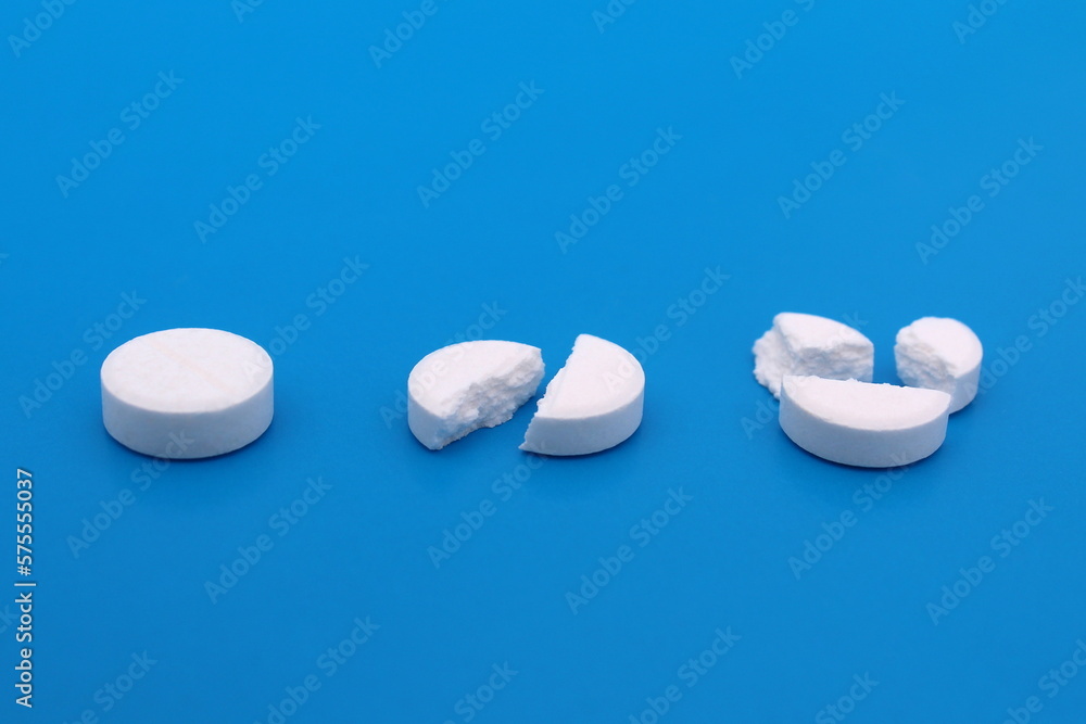 White broken pills lie on a blue background.
White broken pills lie on a blue background.