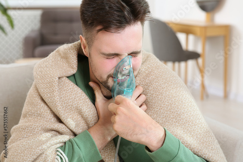 Sick man using nebulizer for inhalation indoors