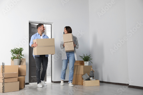 Happy couple with moving boxes entering in new apartment