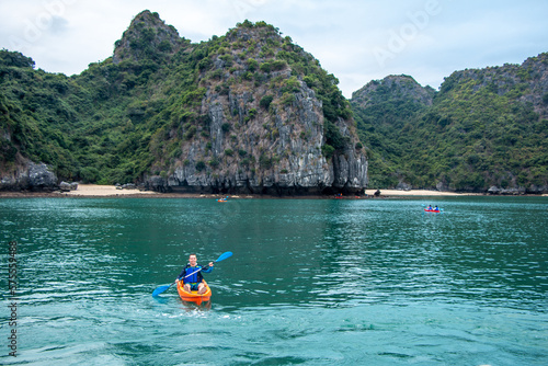 Kayaker on the water in front of a limestone karst island with rainforest and sandy beaches in the Ha Long Bay UNESCO World Heritage site in Qiang Ninh Province in northern Vietnam © QuiBee