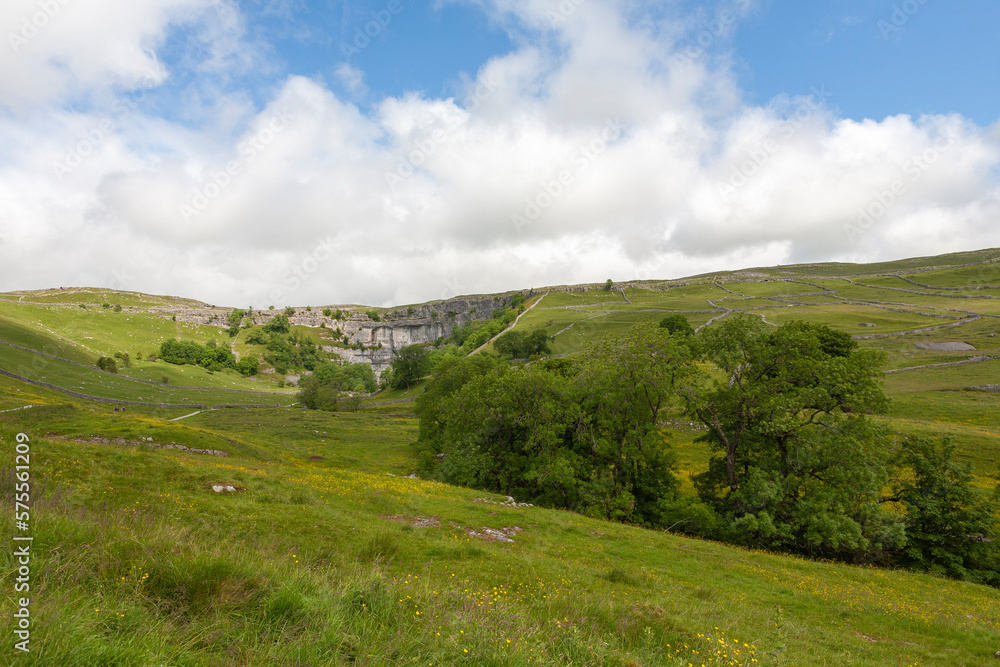 Far view of Malham Cove, with meadows and limestone moorland beyond, Yorkshire Dales National Park, North Yorkshire, UK