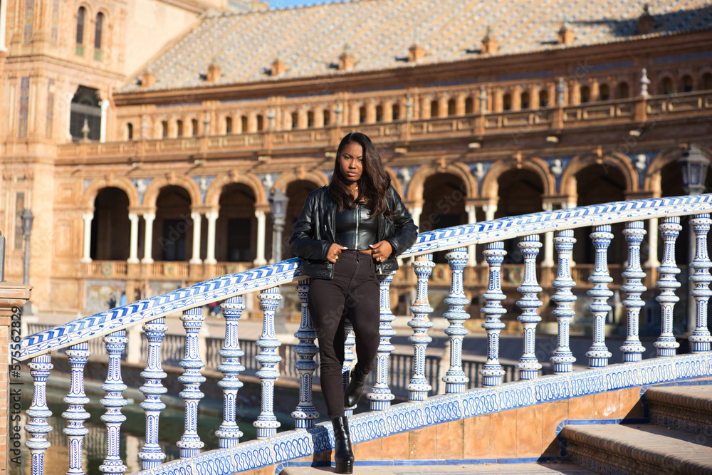 beautiful black latin woman is travel in spain and visits the most important square in the city of seville. The woman is dressed in modern and casual black clothes.