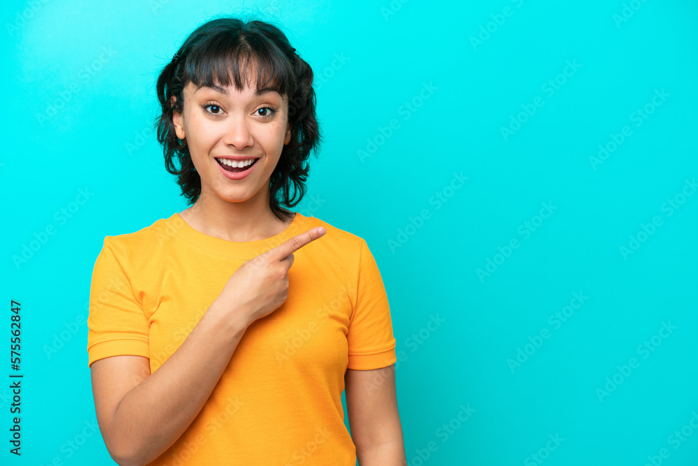 Young Argentinian woman isolated on blue background surprised and pointing side Young Argentinian woman isolated on blue background surprised and pointing side