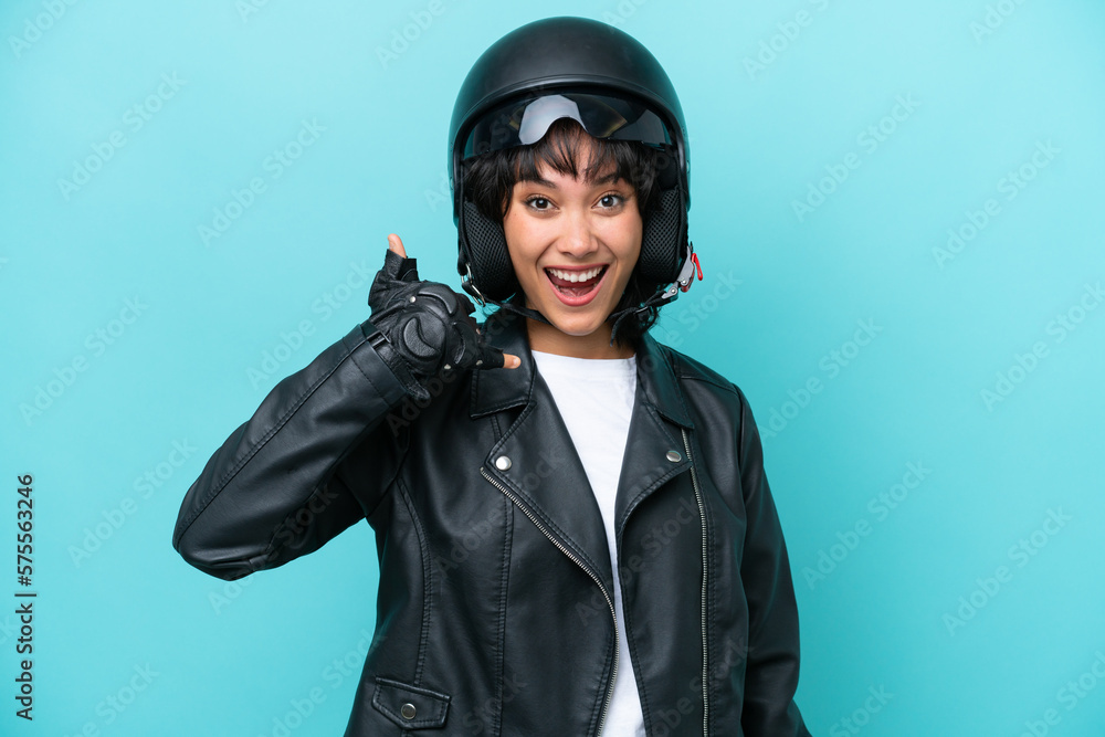 Young Argentinian woman with a motorcycle helmet isolated on blue background making phone gesture. Call me back sign Young Argentinian woman with a motorcycle helmet isolated on blue background making phone gesture. Call me back sign