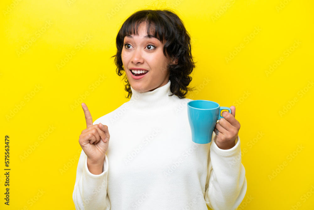 Young Argentinian woman holding cup of coffee isolated on yellow background intending to realizes the solution while lifting a finger up Young Argentinian woman holding cup of coffee isolated on yellow background intending to realizes the solution while lifting a finger up