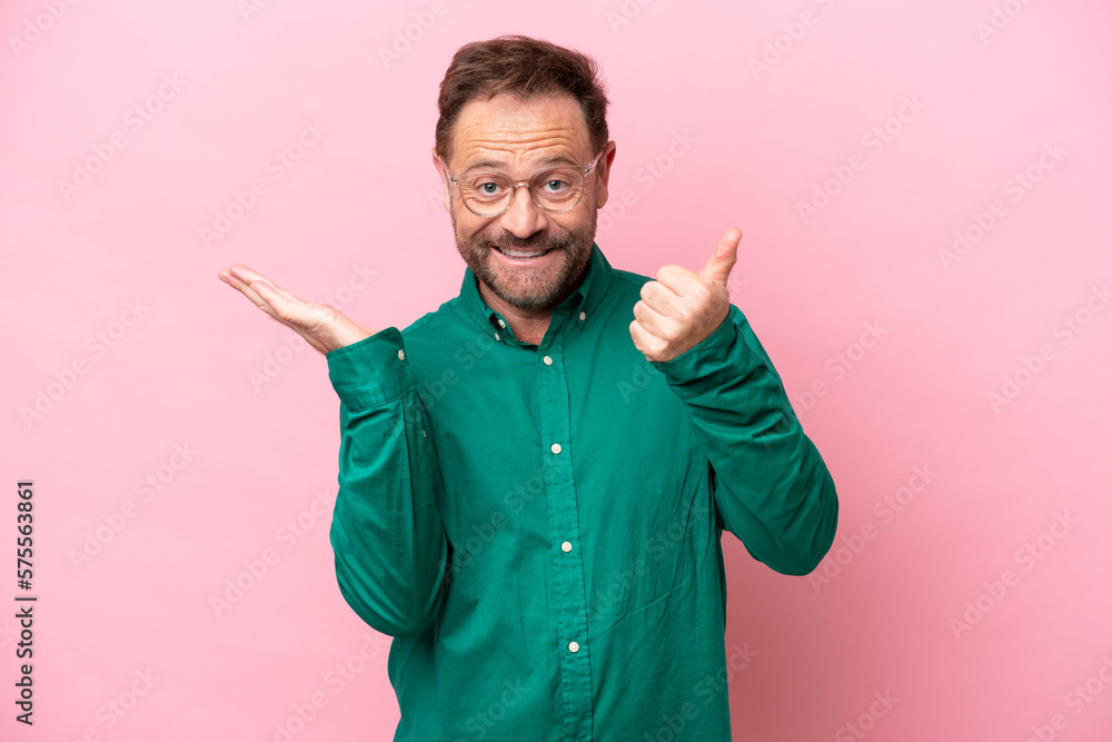 Middle age caucasian man isolated on pink background holding copyspace imaginary on the palm to insert an ad and with thumbs up Middle age caucasian man isolated on pink background holding copyspace imaginary on the palm to insert an ad and with thumbs up