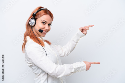 Telemarketer Russian girl working with a headset isolated on white background pointing finger to the side and presenting a product