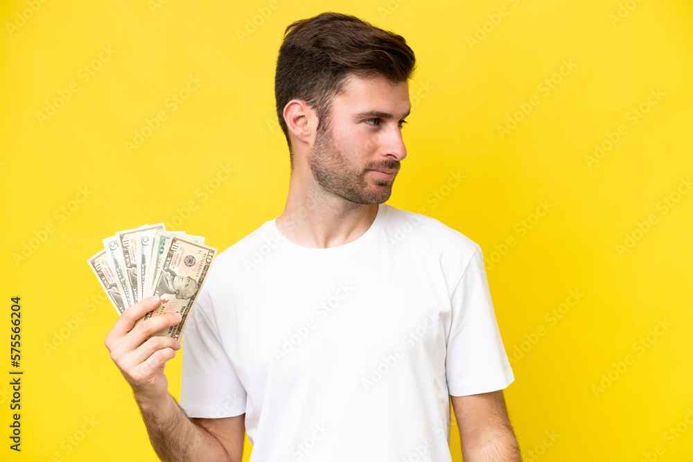 Young caucasian man taking a lot of money isolated on yellow background looking to the side Young caucasian man taking a lot of money isolated on yellow background looking to the side