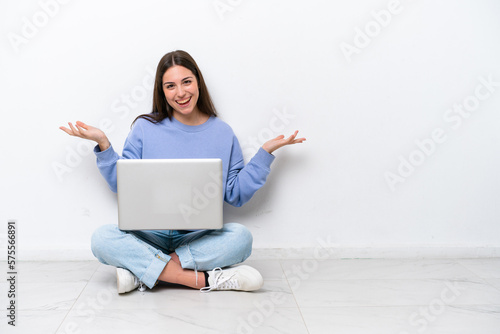 Young caucasian woman with laptop sitting on the floor isolated on white background with shocked facial expression © luismolinero