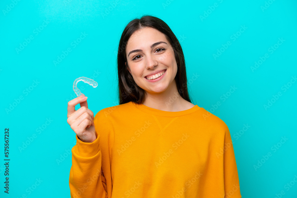 Young caucasian woman holding invisible braces isolated on blue background smiling a lot Young caucasian woman holding invisible braces isolated on blue background smiling a lot