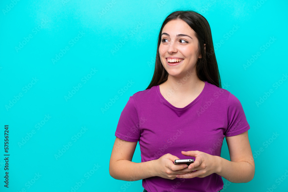 Young girl isolated on blue background using mobile phone and looking up Young girl isolated on blue background using mobile phone and looking up
