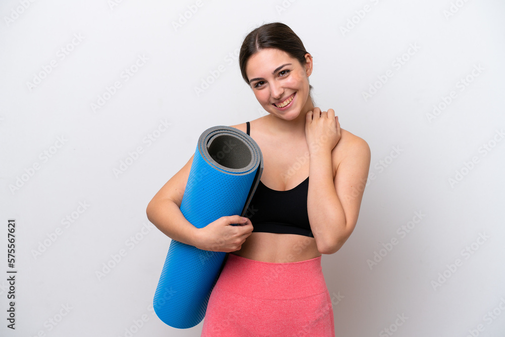 Young sport girl going to yoga classes while holding a mat isolated on white background laughing