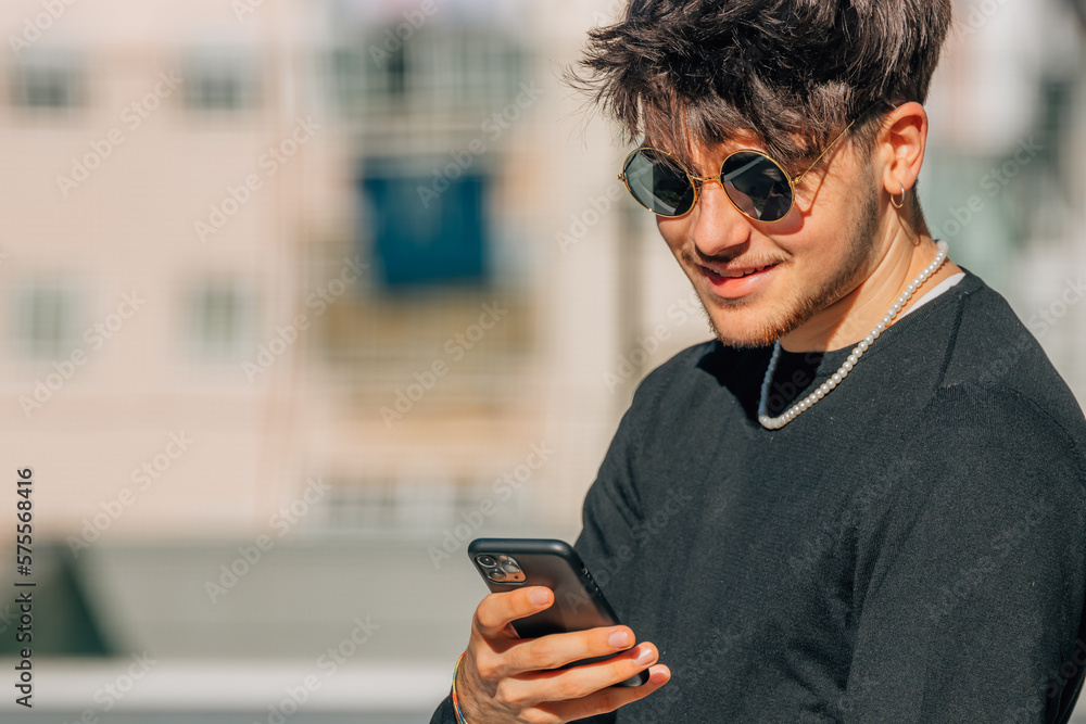 Fototapeta premium young man with sunglasses looking at mobile phone in the street