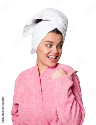 Young caucasian woman in bathrobe isolated points with thumb finger away, laughing and carefree.
