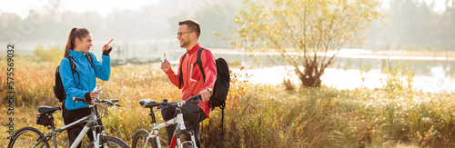 Wide aspect ratio photo of a beautiful young Caucasian couple eating energy bars and talking while taking a break from a mountain bike ride in countryside
