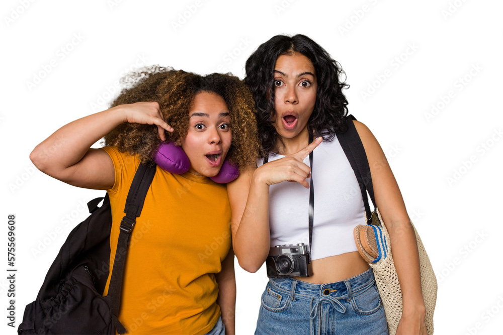Two diverse friends on a beach vacation with vintage camera, beach bag, and travel pillow pointing to the side Two diverse friends on a beach vacation with vintage camera, beach bag, and travel pillow pointing to the side