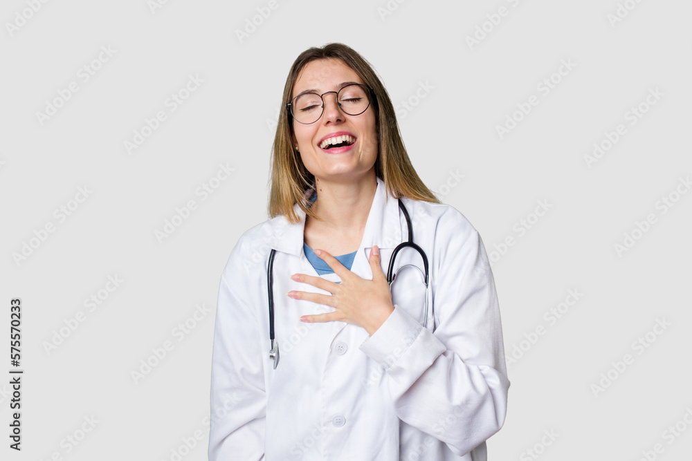 Compassionate female physician with a stethoscope around her neck, ready to diagnose and care for her patients in her signature white coat laughs out loudly keeping hand on chest. Compassionate female physician with a stethoscope around her neck, ready to diagnose and care for her patients in her signature white coat laughs out loudly keeping hand on chest.