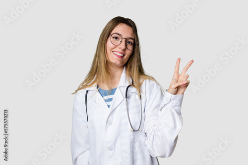 Compassionate female physician with a stethoscope around her neck  ready to diagnose and care for her patients in her signature white coat joyful and carefree showing a peace symbol with fingers.
