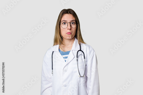 Compassionate female physician with a stethoscope around her neck  ready to diagnose and care for her patients in her signature white coat shrugs shoulders and open eyes confused.