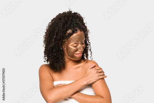 Young african american curly woman wearing a towel and a facial mask isolated
