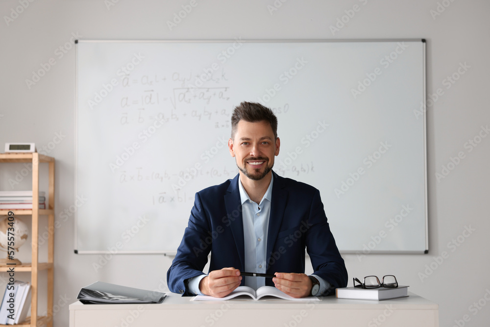 Happy teacher sitting at table in classroom Happy teacher sitting at table in classroom
