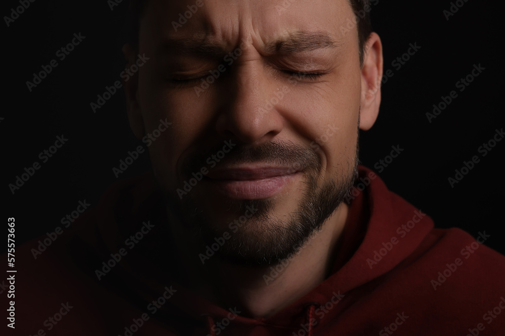 Sad man crying on black background, closeup