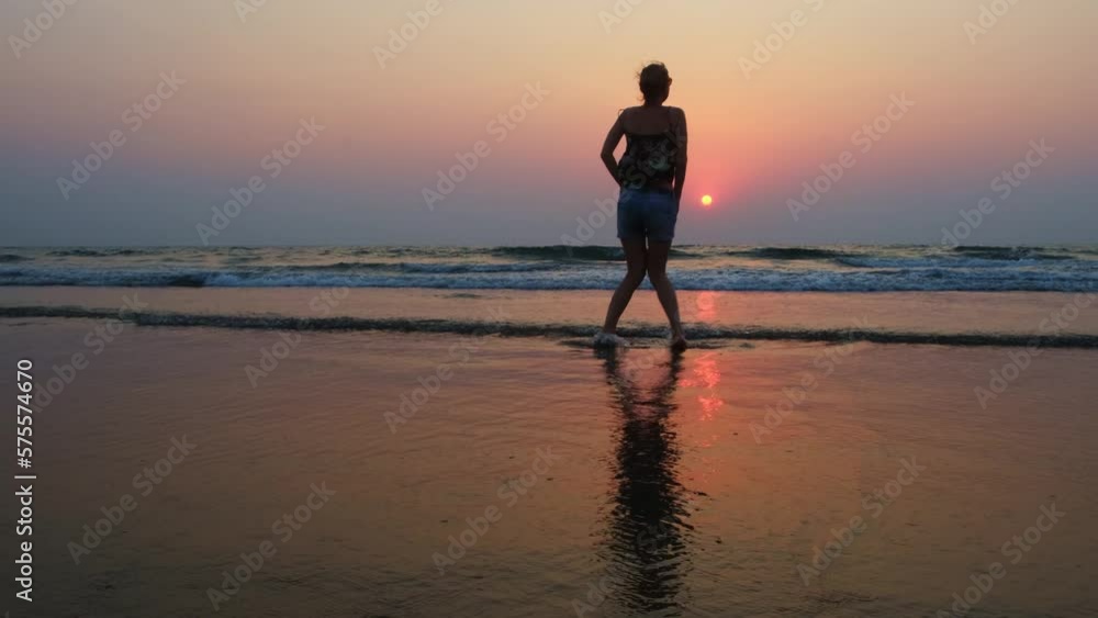 Happy woman dancing in waves on the seacoast at sunset. Silhouette of young female tourist having fun during summer vacation on the sea. Happy woman dancing in waves on the seacoast at sunset. Silhouette of young female tourist having fun during summer vacation on the sea.