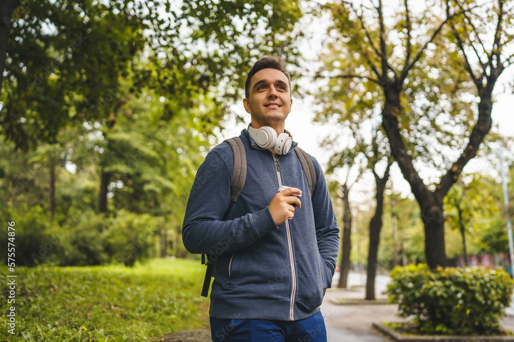 One young adult caucasian man walking in the city or town near park with cup of coffee in autumn or spring day happy male tourist standing alone real people copy space One young adult caucasian man walking in the city or town near park with cup of coffee in autumn or spring day happy male tourist standing alone real people copy space