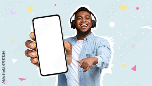 Photographie Happy black man using headphones, showing smartphone, mockup