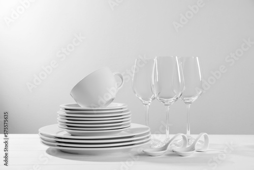Set of clean dishware and glasses on white wooden table against light background